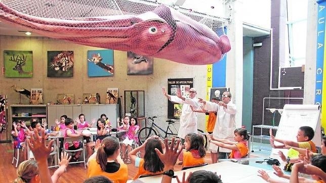 Un grupo de niños aprende en una aula del museo, bajo una maqueta del calamar gigante