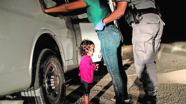La niña Yanelaa, de Honduras, llora mientras su madre es cacheada por un policía de fronteras
