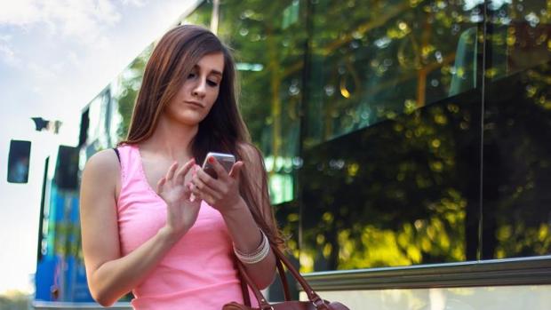 Una joven mira el móvil mientras camina por la calle