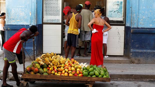 Un hombre empuja un carro de fruta frente a una tienda, donde se aprecia la foto de Raúl Castro