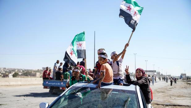 Varias personas ondean banderas sirias revolucionarias durante una protesta en la provincia de Idlib