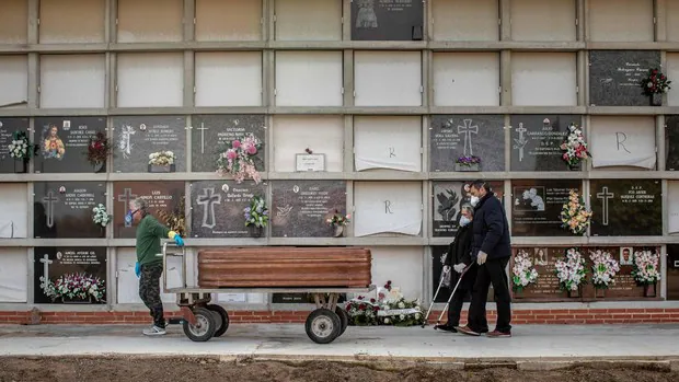Un operario de un cementerio de València traslada un féretro seguido por los familiares